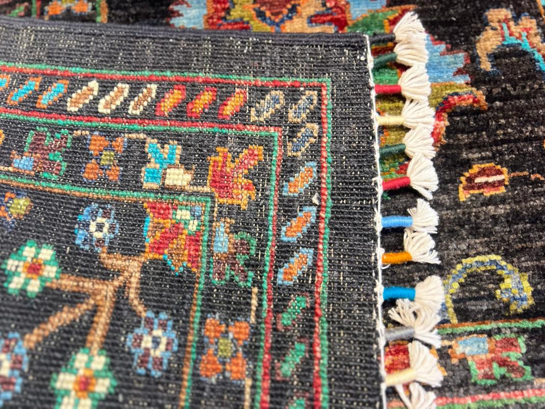 Extreme close-up of the Chobi Sultani Afghan carpet – thousands of hand-tied wool knots visible in vivid teal, crimson, gold and ivory, with the layered border and hand-knotted cotton fringe showcasing the density and precision of Jawzjan craftsmanship