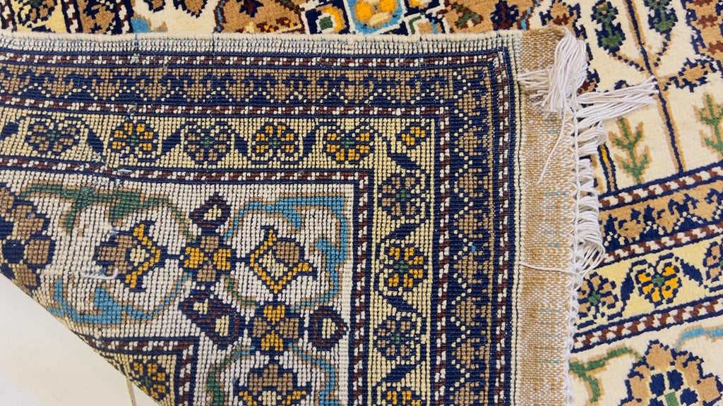 Macro close-up of hand-knotted underside of Belzhiki Gandumak Afghan carpet – showing individual knot density and weave structure, navy blue border with antique gold floral motifs, teal medallion detail, natural cotton fringe, evidence of 40×40 knots per 10cm craftsmanship, Sheberghan Afghanistan