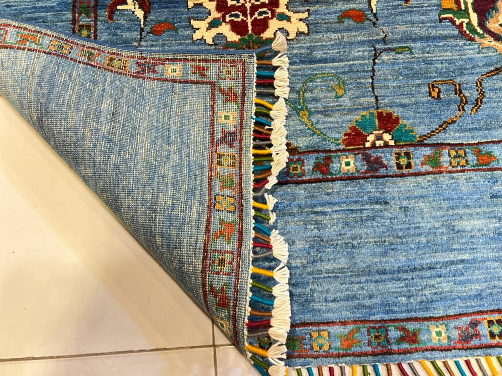 Folded corner of a Chobi Sultani Afghan carpet revealing the flat reverse weave and vibrant multi-colored hand-tied fringe — authenticating 100% hand-knotted natural wool construction, Golden Loom Afghanistan