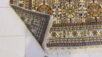 Corner detail of Belzhiki Gandumak hand-knotted Afghan carpet showing the reverse side fold – ivory field with geometric Gandumak pattern, multi-stripe border in navy, teal, gold and sage green, white hand-knotted fringe, Sheberghan Afghanistan