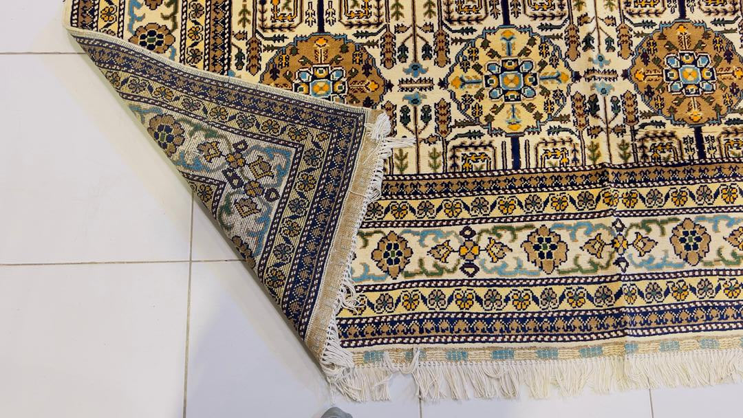 Corner detail of Belzhiki Gandumak hand-knotted Afghan carpet showing the reverse side fold – ivory field with geometric Gandumak pattern, multi-stripe border in navy, teal, gold and sage green, white hand-knotted fringe, Sheberghan Afghanistan