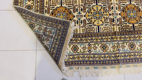 Corner detail of Belzhiki Gandumak hand-knotted Afghan carpet showing the reverse side fold – ivory field with geometric Gandumak pattern, multi-stripe border in navy, teal, gold and sage green, white hand-knotted fringe, Sheberghan Afghanistan