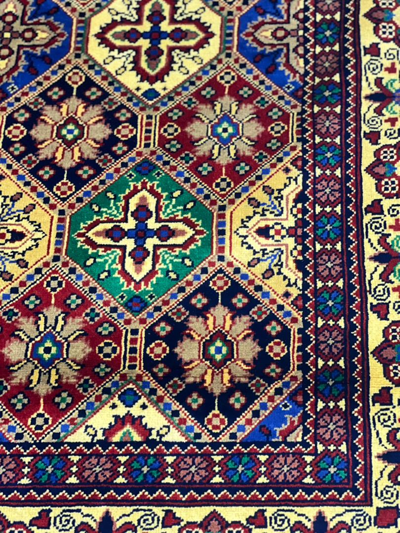 Close-up of Belzhiki Afghan carpet tile design — hand-knotted cross and floral medallions in emerald green, navy and burgundy, showing 40x40 knot density per 10cm