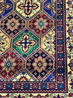 Close-up of Belzhiki Afghan carpet tile design — hand-knotted cross and floral medallions in emerald green, navy and burgundy, showing 40x40 knot density per 10cm