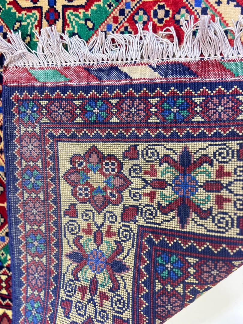 Detail of Belzhiki Afghan carpet fringe and ivory border — hand-knotted floral scrollwork in red, blue and green, showing fine craftsmanship and tight weave structure