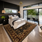 A luxury bedroom featuring a large traditional oriental area rug with a dark red, gold, and black pattern on light wood floors. The room has a modern black accent wall, a bed with neutral-toned bedding, and large glass sliding doors looking out to a balcony and green trees.