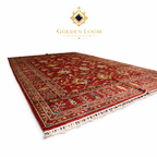 Hand-knotted Afghan carpet in crimson red with multicolor botanical motifs and ivory fringe, angled view showing pile depth — Golden Loom Afghanistan