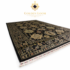 Angled view of a hand-knotted Afghan wool rug with black field, ivory floral border, and knotted fringe detail