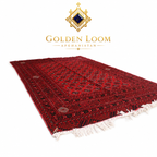 A red Persian-style area rug with intricate black and gold geometric patterns and white fringe, displayed on a clean white background with the Golden Loom Afghanistan brand logo above it.
