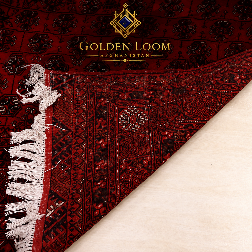 A close-up of a dark red and black patterned rug with white fringe, shown folded over on a light beige surface. The brand name 'Golden Loom Afghanistan' is printed at the top.