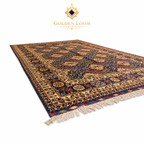 Angled view of large Afghan handwoven area rug with navy, burgundy, and gold geometric floral design on white background