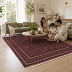 Family relaxing on the floor of a bright Scandinavian-style living room on a large hand-knotted Afghan rug in deep red with geometric repeat pattern and cream fringe — Golden Loom Afghanistan