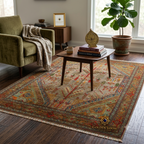 Afghan handwoven rug with tree-of-life and botanical motifs in sage and red, styled in a mid-century reading nook with velvet armchair