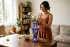 Woman smiling while arranging wildflowers in a handmade Golden Loom Afghanistan lapis lazuli mosaic vase on a wooden dining table — Afghan artisan home décor in a bright living room