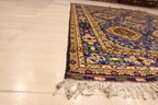 A detailed side angle view of a traditional Persian rug featuring intricate blue and yellow geometric patterns with white fringe tassels on a light-colored tile floor