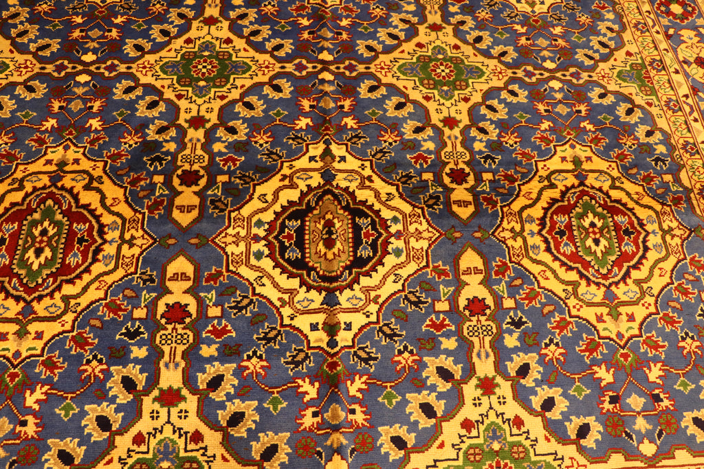 A high-angle, close-up shot showing the detailed, symmetrical geometric pattern of an oriental carpet dominated by vibrant blue, yellow, red, and green colors
