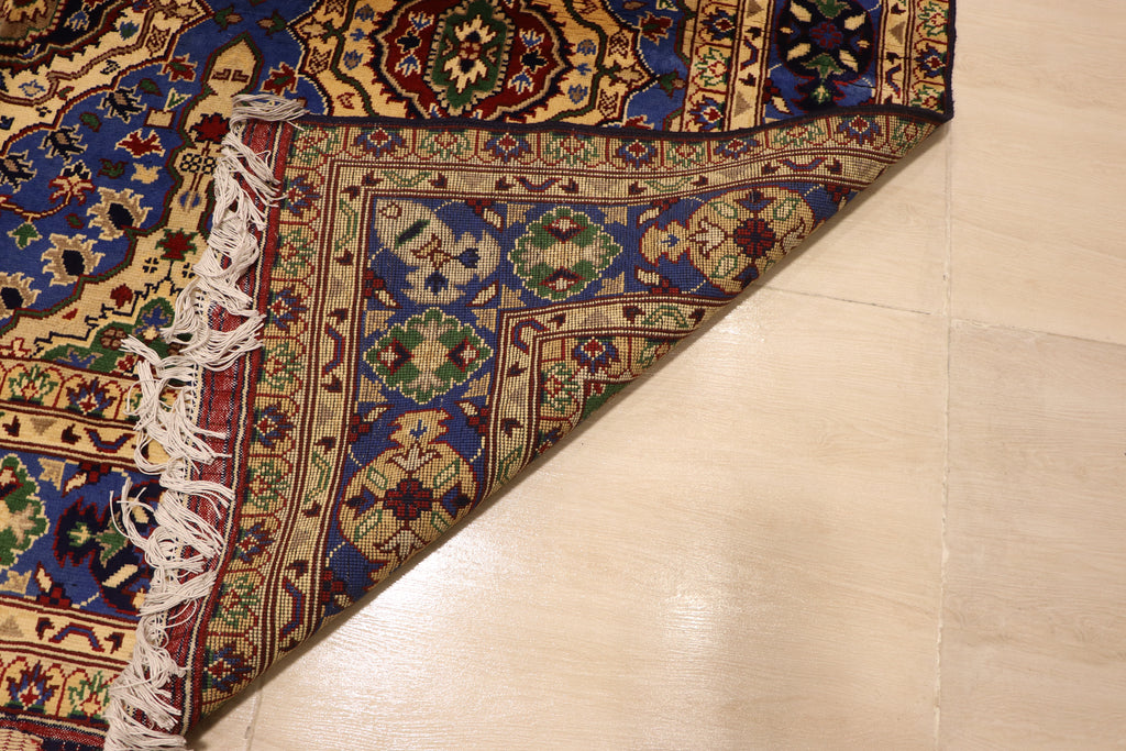 A corner of a hand-knotted Persian rug folded back to display the high-quality weave of the underside, resting on a beige tiled floor