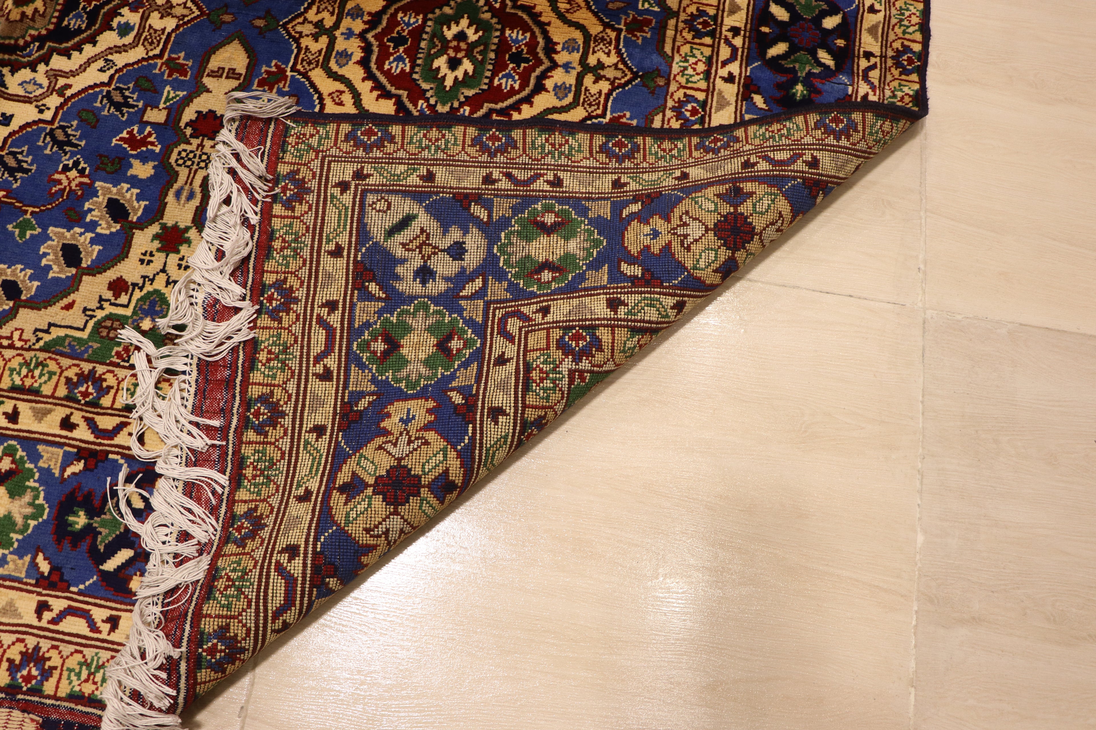A corner of a hand-knotted Persian rug folded back to display the high-quality weave of the underside, resting on a beige tiled floor