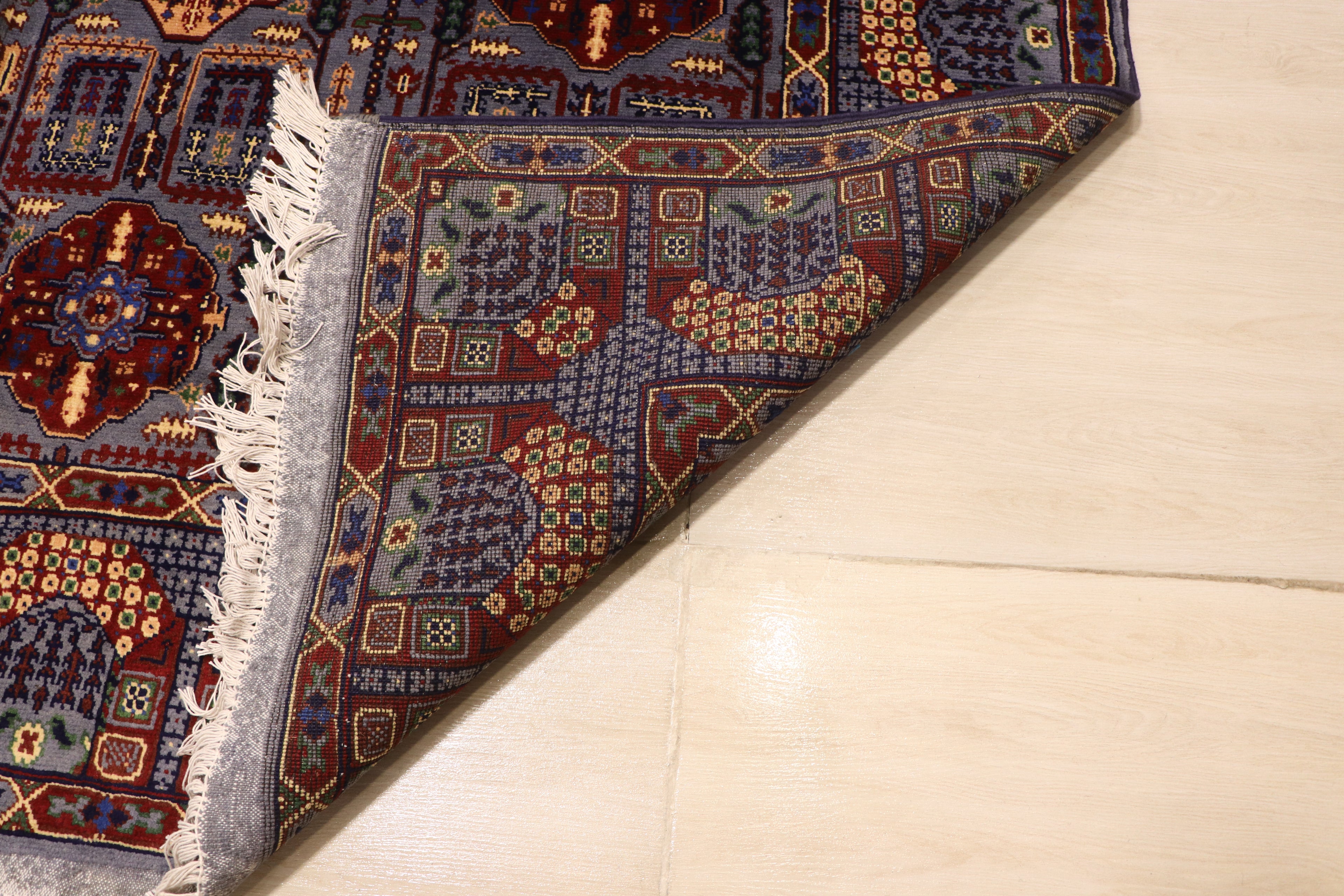 Close-up of the back of a hand-knotted Afghan rug, showing the detailed weave and quality craftsmanship of the intricate blue, red, and gold floral design