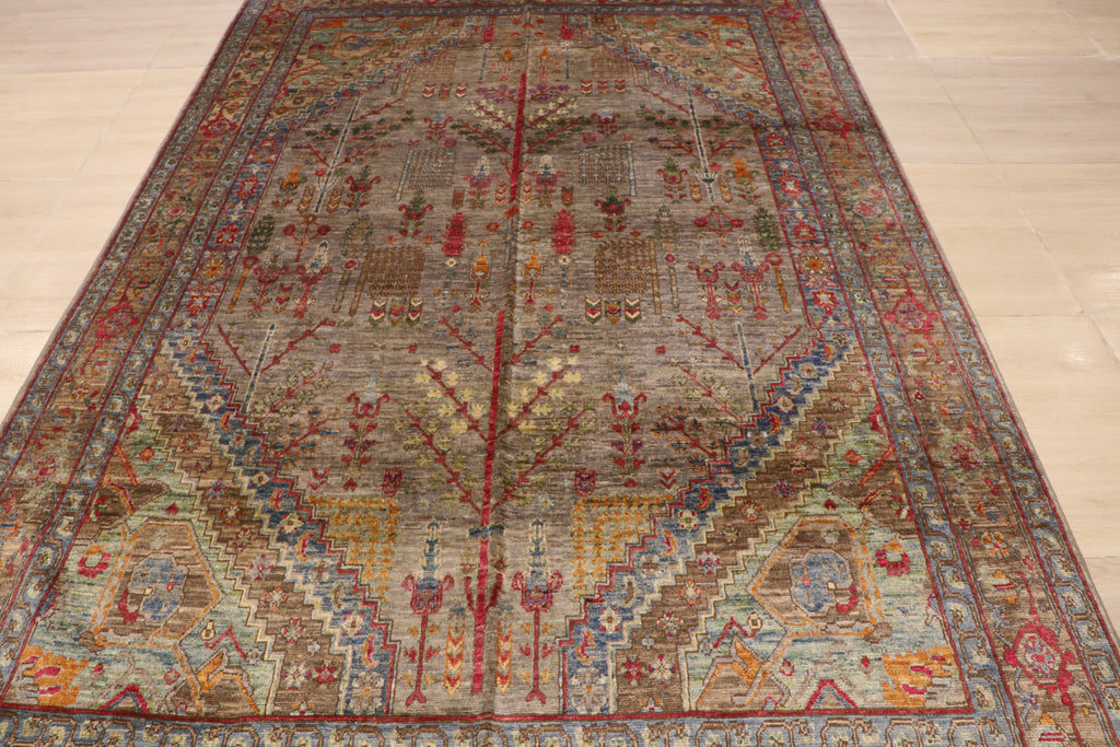 Close-up of handwoven Afghan rug featuring symmetrical tree-of-life and floral motifs on a warm grey field with crimson and gold accents