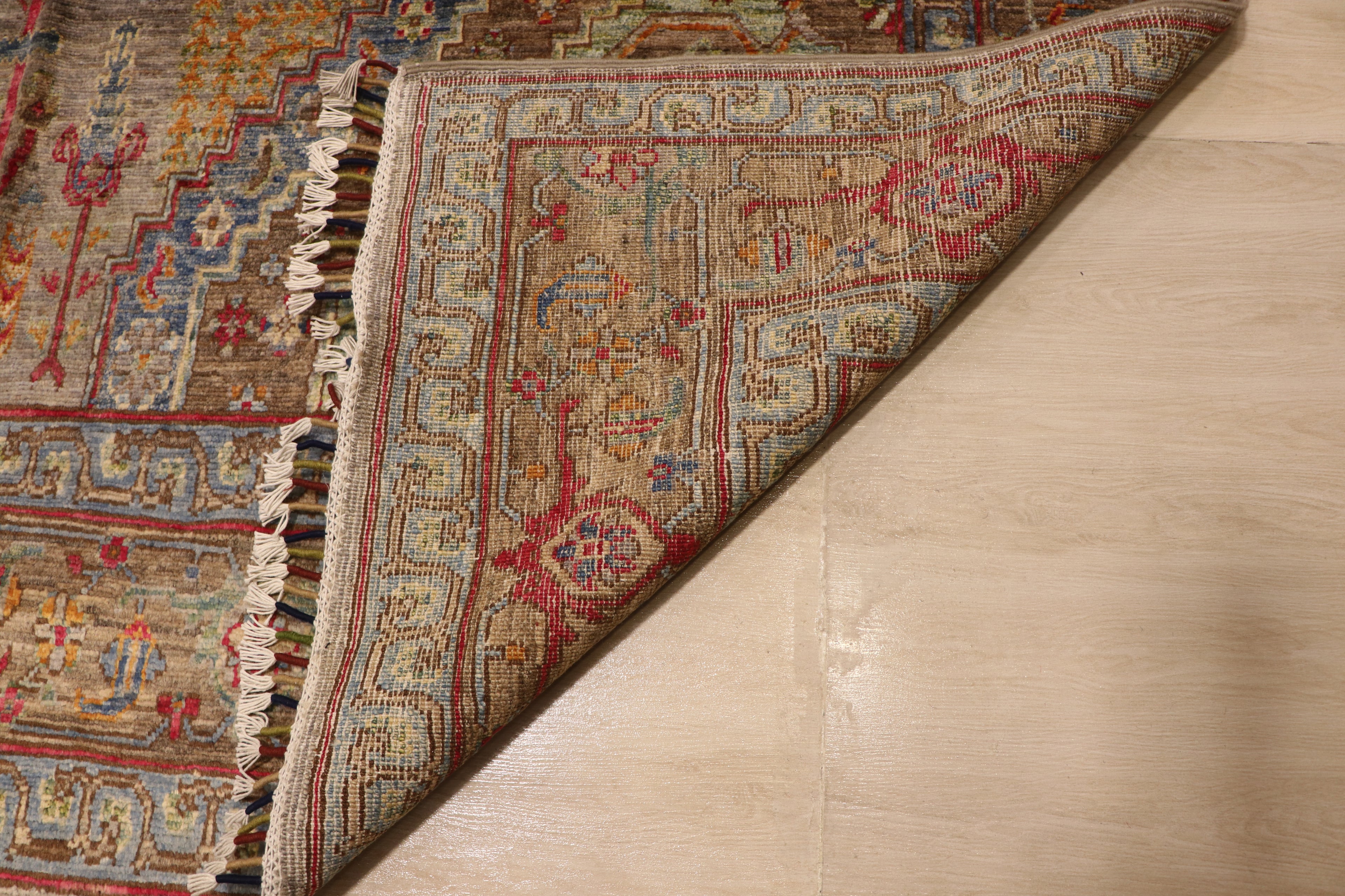 Detail of handwoven Afghan carpet corner folded back revealing dense knotted reverse with intricate border pattern in red, blue, and taupe