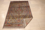 Full view of handwoven Afghan carpet with grey-taupe field, all-over botanical motifs, and multicolor geometric border, corner folded to show reverse