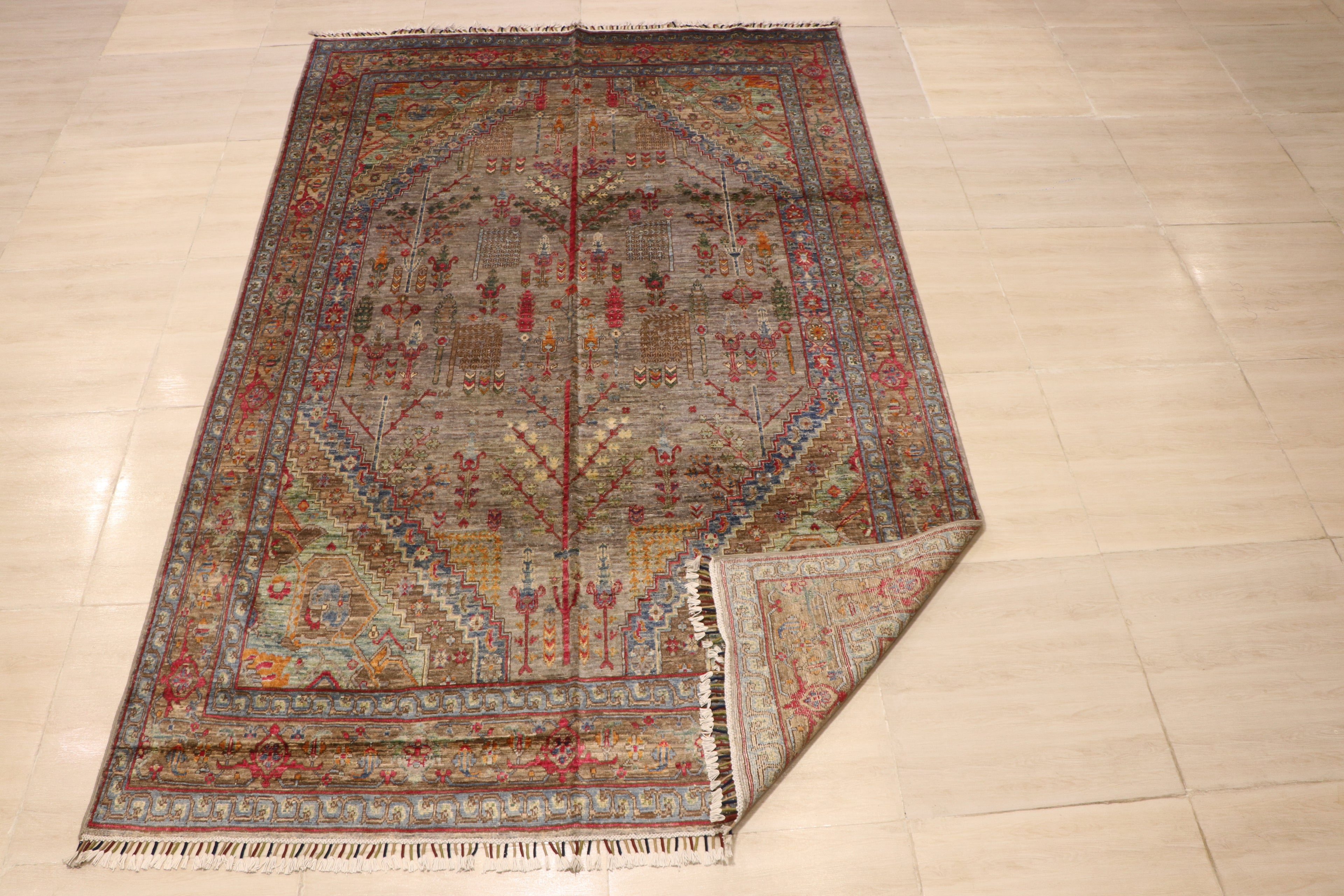 Full view of handwoven Afghan carpet with grey-taupe field, all-over botanical motifs, and multicolor geometric border, corner folded to show reverse