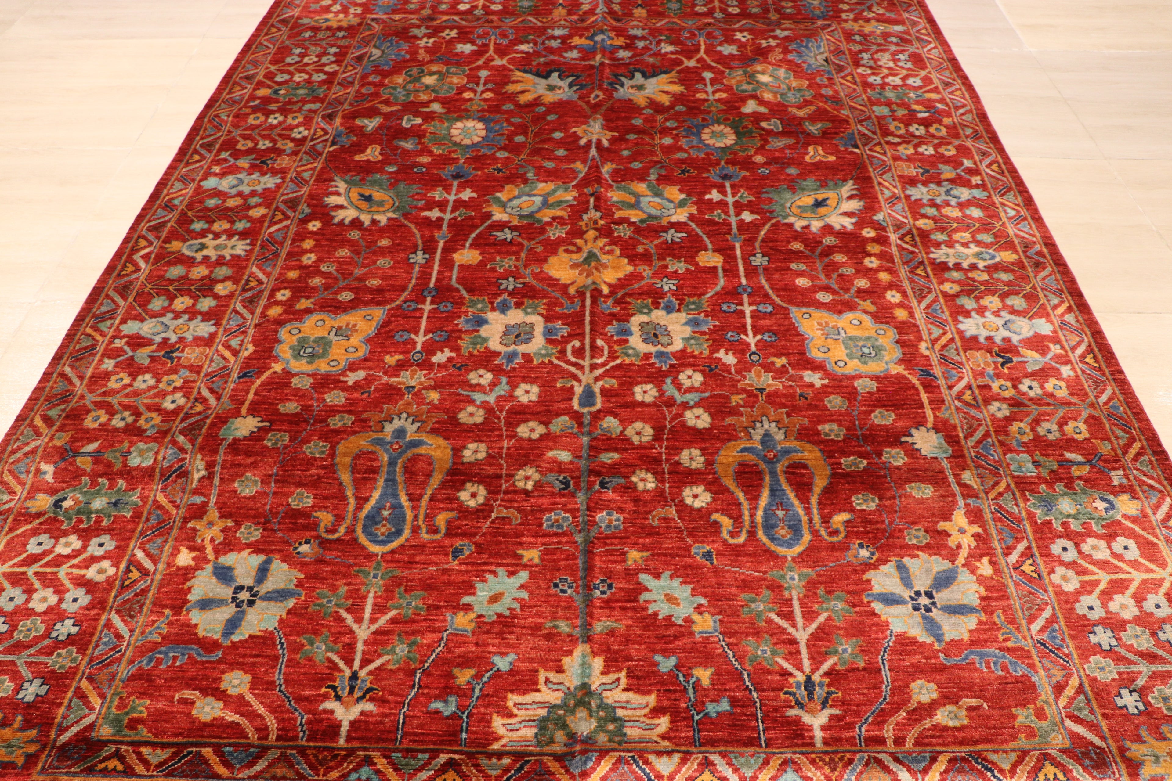 Low-angle view of Afghan hand-knotted red Chobi carpet showing full floral field pattern, geometric border, and natural wool texture on light floor — Golden Loom Afghanistan