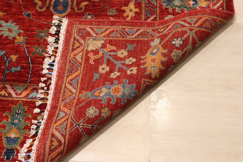 Close-up of Afghan hand-knotted Chobi rug corner fold showing dense wool pile, hand-tied fringe, and multicolor floral border detail — Golden Loom Afghanistan