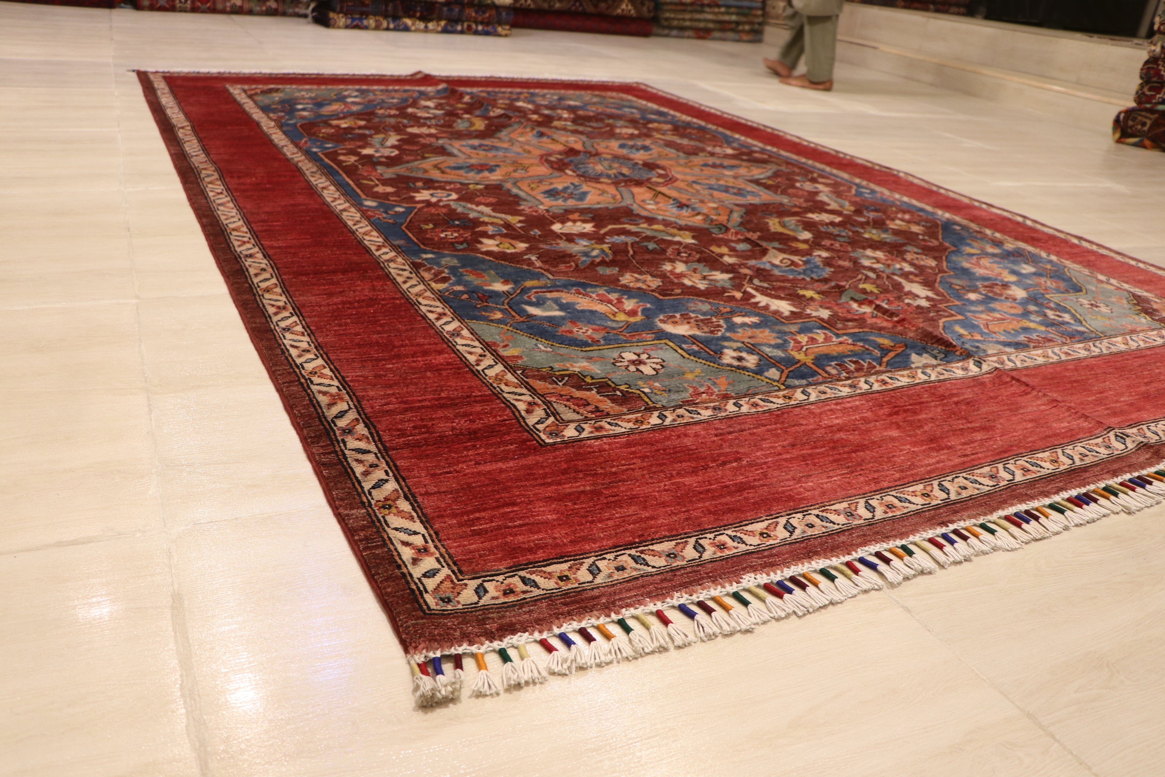 Full view of Chobi Kashan Afghan hand-knotted wool carpet laid flat on white floor, showing red field, blue border, and ivory fringe
