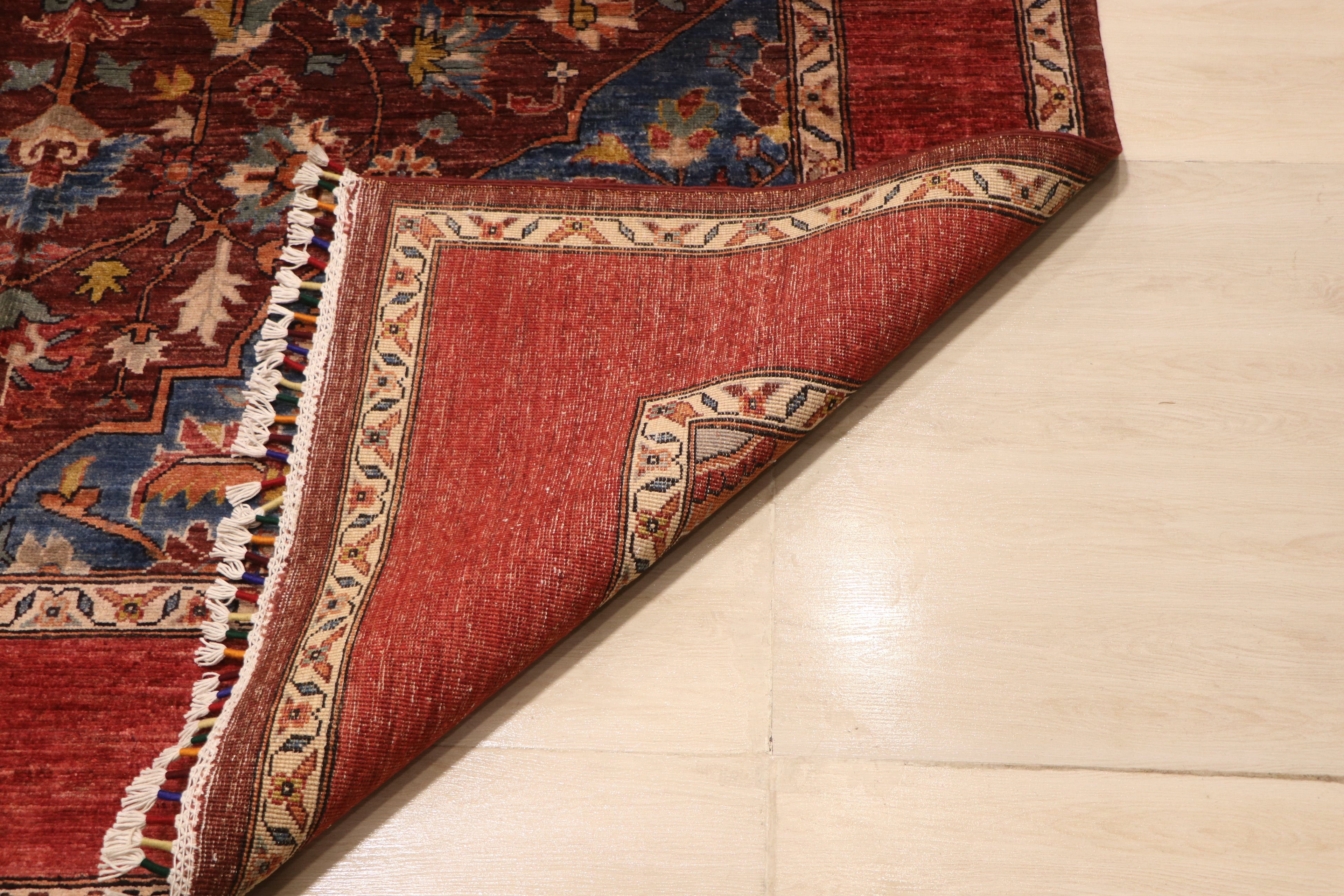 Folded corner of Chobi Kashan Afghan carpet revealing hand-knotted wool backing with ivory and red border detail