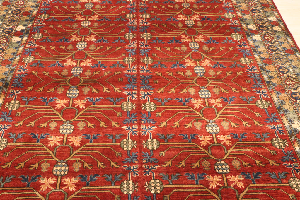 Close-up of Sultani Chobi hand-knotted Afghan carpet showing crimson red field with geometric lattice pattern, botanical motifs in gold, blue, and blush pink, with multi-layered border
