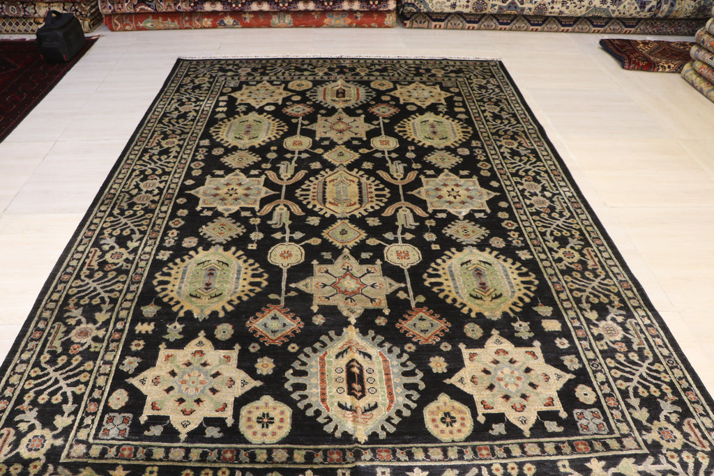 Hand-knotted Afghan area rug with black ground and traditional floral medallion design, displayed on showroom floor