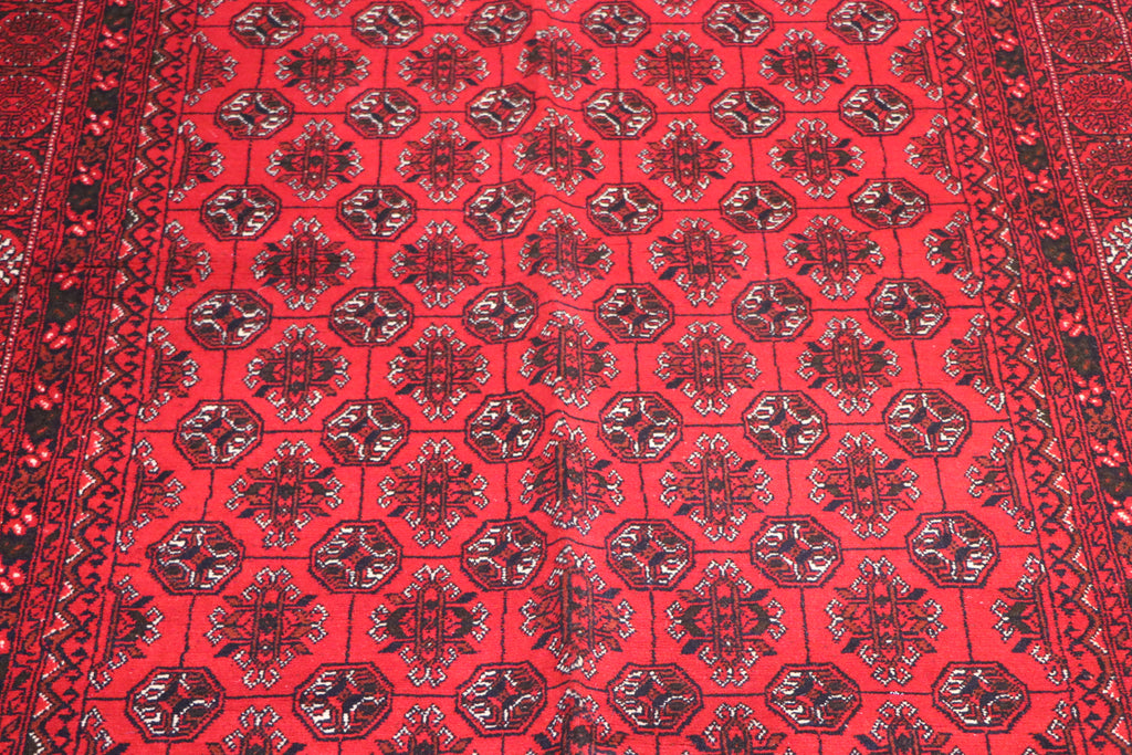 A close-up of a red patterned rug with repeating dark medallion motifs and a decorative border.