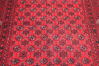 A close-up of a red patterned rug with repeating dark medallion motifs and a decorative border.