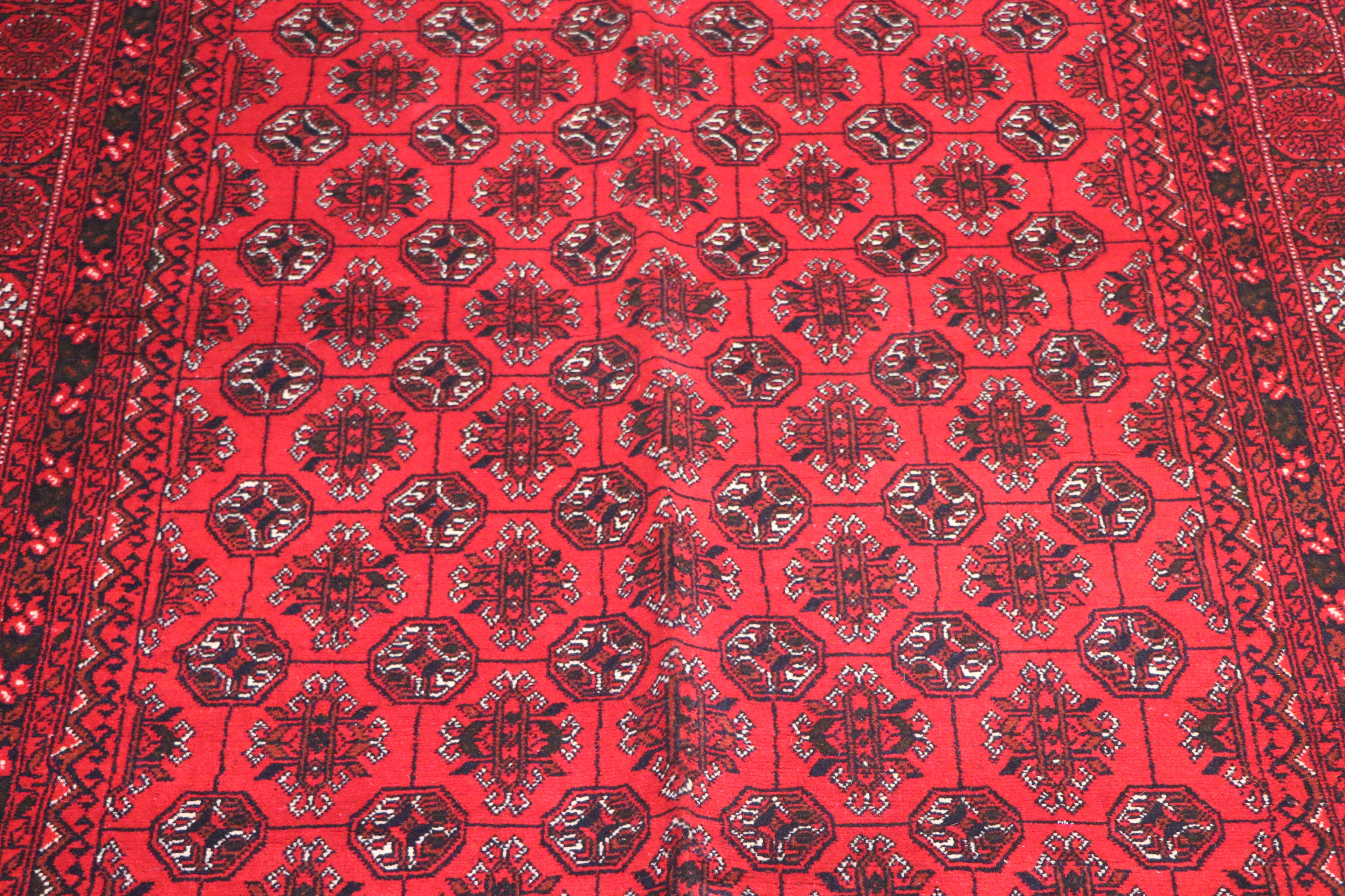 A close-up of a red patterned rug with repeating dark medallion motifs and a decorative border.