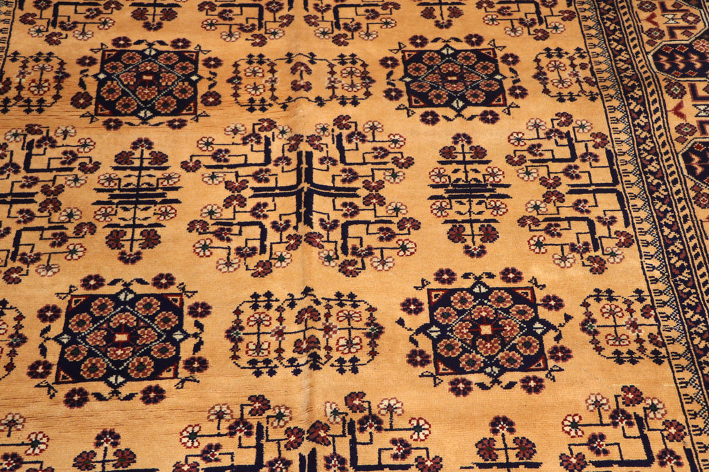 A close-up of a patterned rug with a warm tan background and dark navy and brown geometric floral motifs.