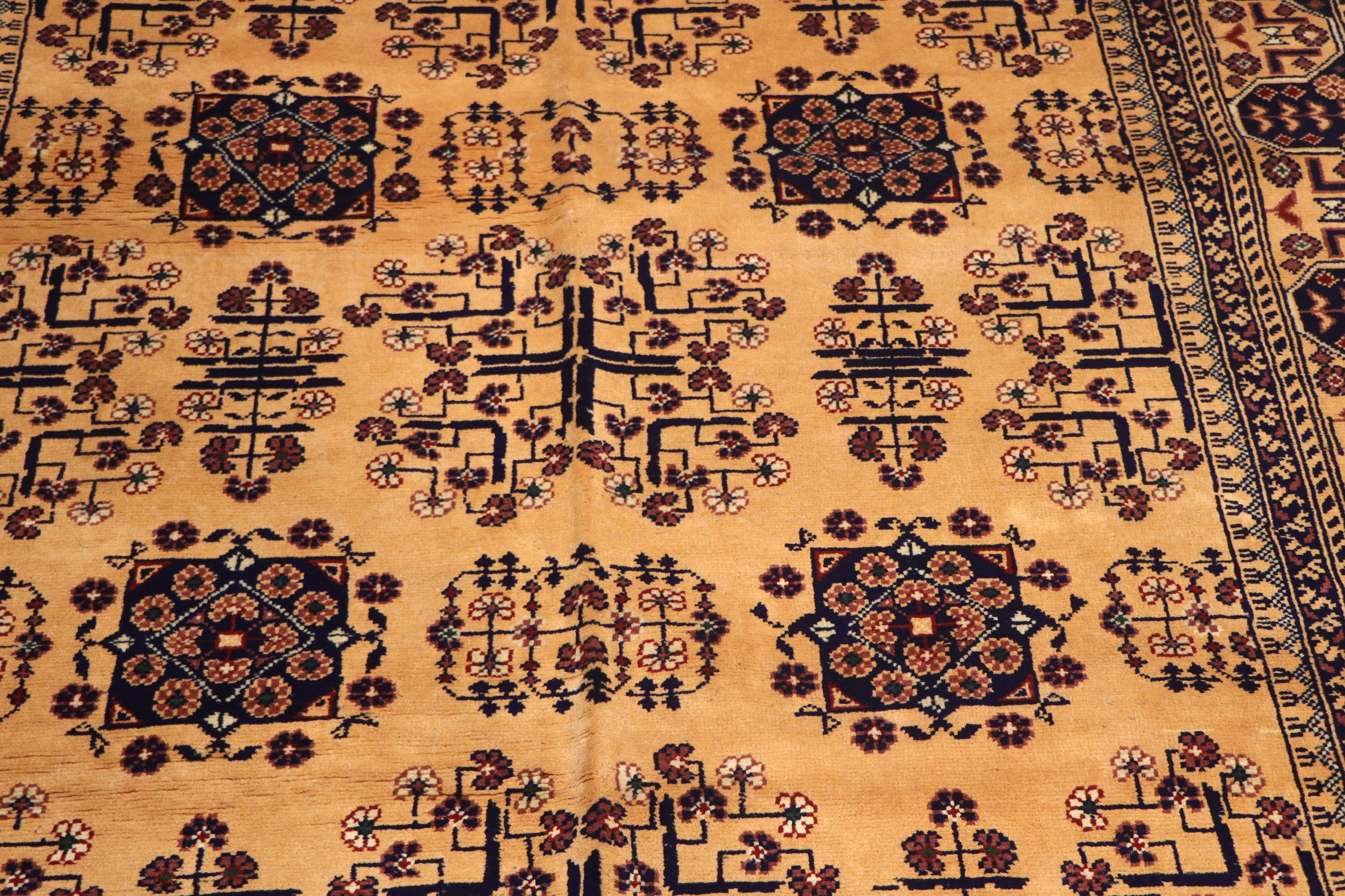 A close-up of a patterned rug with a warm tan background and dark navy and brown geometric floral motifs.