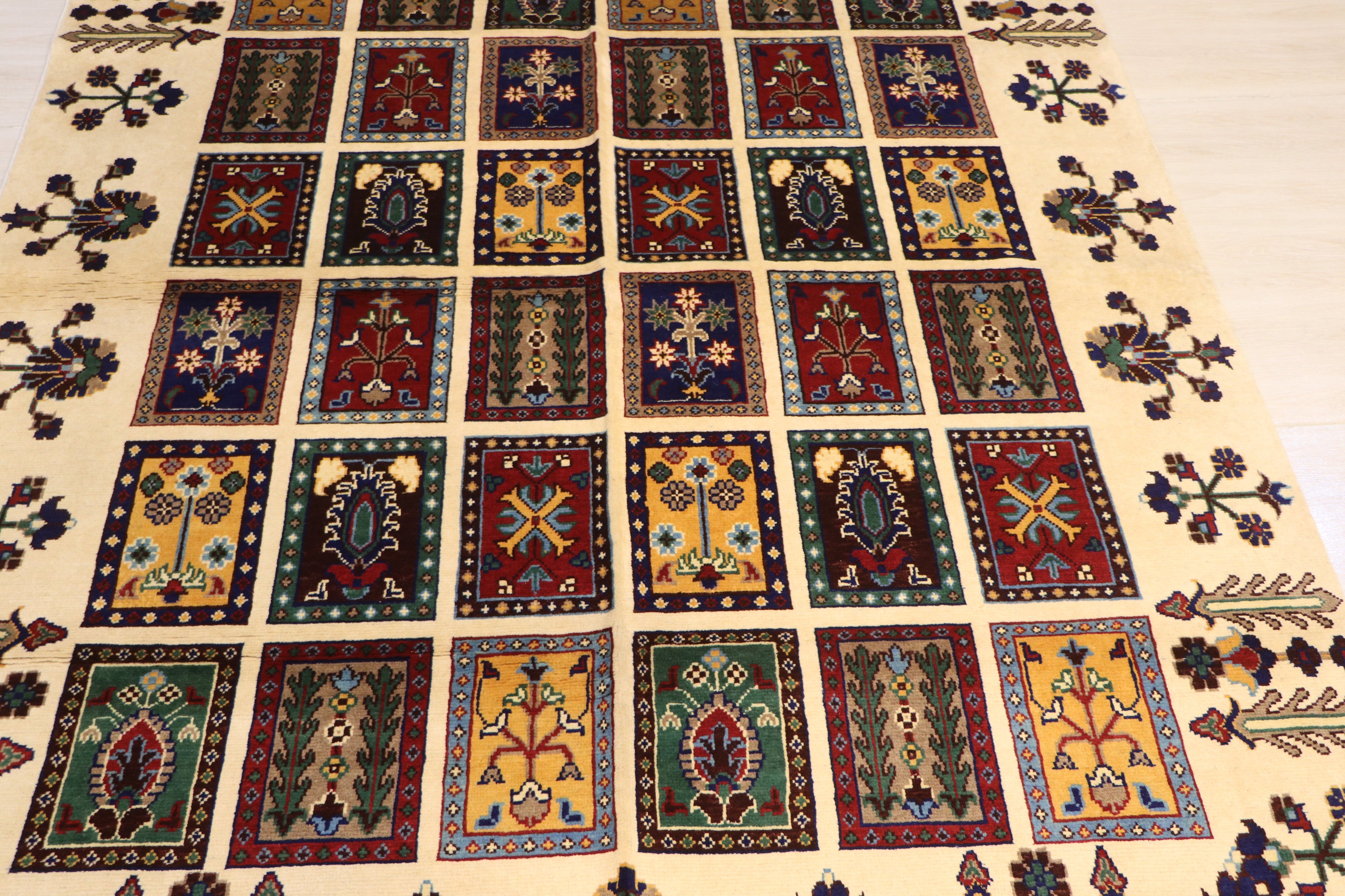 A large traditional Persian-style area rug laid flat on a light-colored floor, featuring a grid of small colorful rectangular motifs with floral and geometric designs on a cream background.