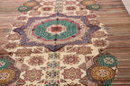 A detailed view of a traditional Afghan-style area rug featuring a large central medallion with intricate geometric and floral patterns in beige, teal, brown, and rust tones.