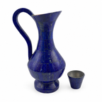 Blue lapis lazuli jug and matching cup displayed on a walnut console beside a window in an ivory interior.