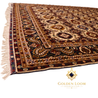 Angled view of large hand-knotted Afghan area rug with all-over geometric medallion field and multi-band paisley border in burgundy and cream