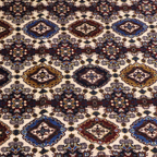 Detailed pile shot of Afghan hand-knotted rug showing repeating diamond gul medallions in burgundy, navy blue, ivory, and olive on cream ground