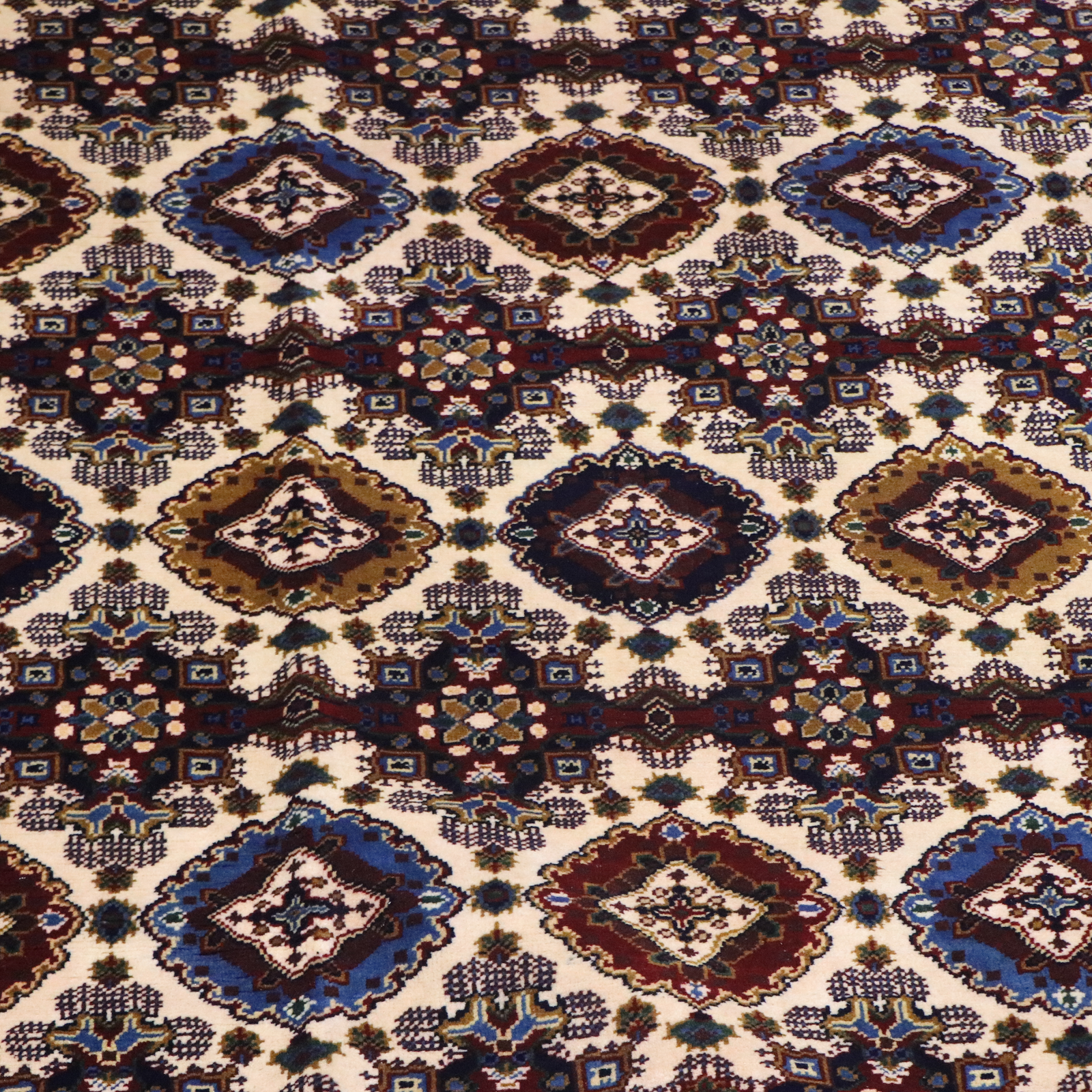 Detailed pile shot of Afghan hand-knotted rug showing repeating diamond gul medallions in burgundy, navy blue, ivory, and olive on cream ground