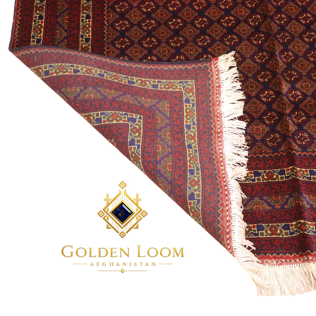 Folded Afghan carpet showing reverse side and intricate multi-border detail with navy, gold, and crimson geometric patterns — Golden Loom Afghanistan