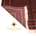Folded Afghan carpet showing reverse side and intricate multi-border detail with navy, gold, and crimson geometric patterns — Golden Loom Afghanistan