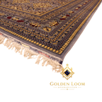 Angled side view of hand-knotted Afghan carpet highlighting multi-layered gold and navy border with ivory knotted fringe on white background