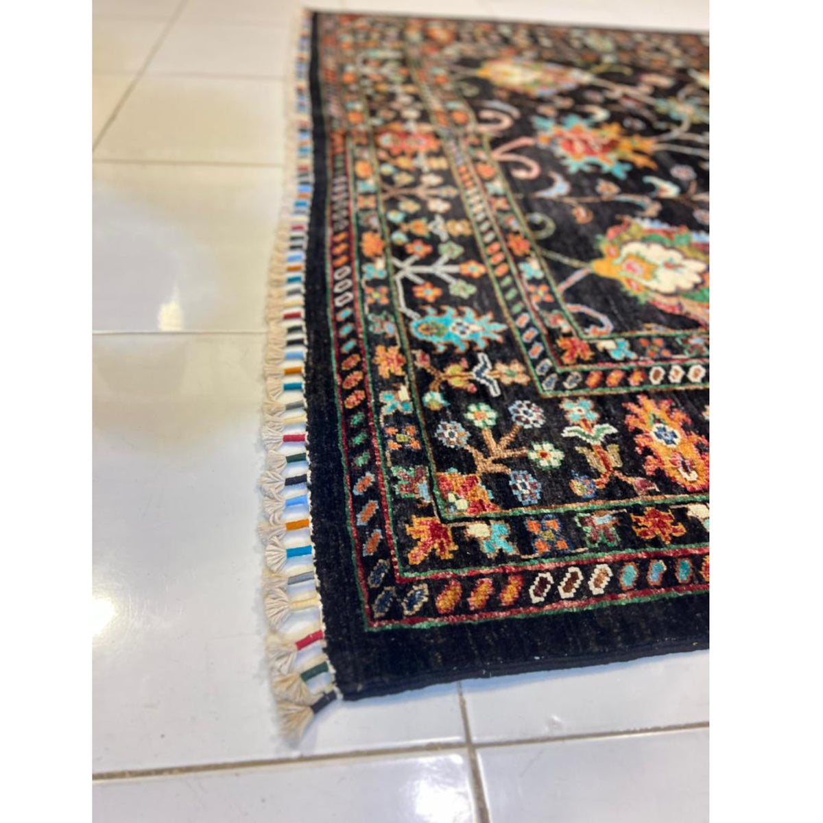 Close-up of the black Afghan wool carpet showing its multicoloured fringe, floral border and hand-knotted pile