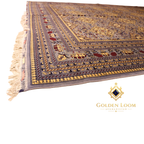Low-angle perspective of hand-knotted Afghan carpet corner showing layered geometric border in gold, navy, and grey with ivory fringe detail
