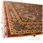 Corner detail of a hand-knotted Afghan rug showing layered ivory and crimson borders with floral motifs, slate blue field, and hand-tied ivory fringe